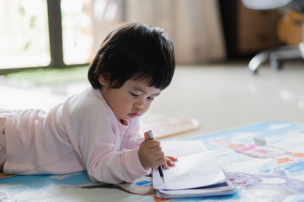 Lindo bebé dibujando en el cuaderno en el suelo