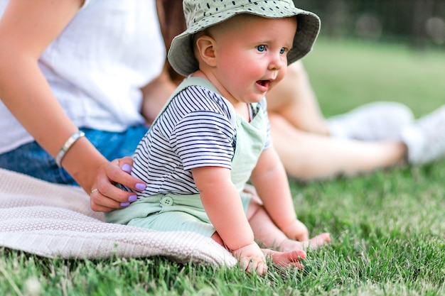 Lindo bebé divertido en estilo casual se sienta en la hierba verde con su infancia concepto de mamá