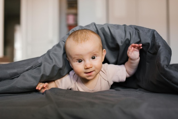 Lindo bebé está acostado boca abajo apoyado en sus muñecas debajo de la manta
