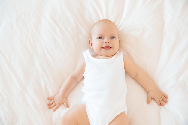 Lindo bebé está acostado en la cama en el dormitorio sonriendo