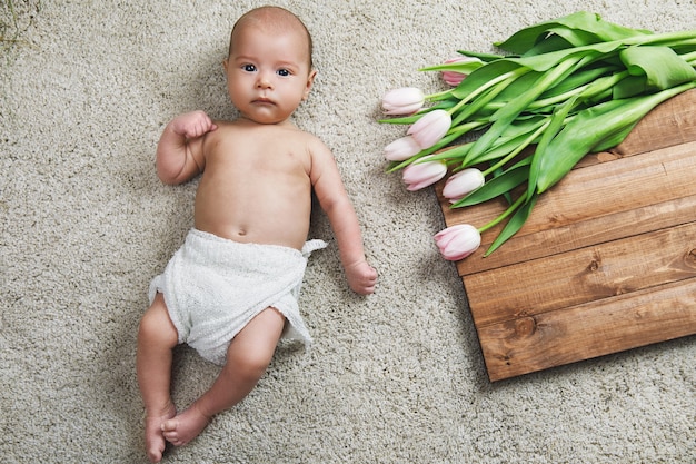 Lindo bebé está acostado en el suelo junto al ramo de flores de tulipanes y tablero de madera