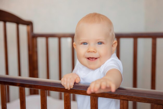 Un lindo bebé está sentado en una cuna, el bebé está sentado en una cuna sonriendo concepto de infancia