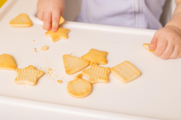 Un lindo bebé está sentado en una silla para niños comiendo galletas Fondo amarillo Espacio de comida para bebés para texto