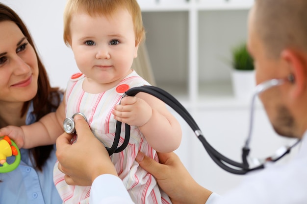 Lindo bebé feliz con su madre en el examen de salud en el consultorio del médico