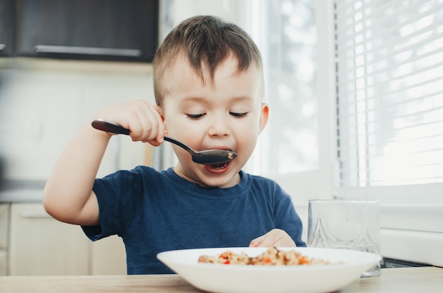 Lindo bebê fofo comendo arroz com uma colher na cozinha