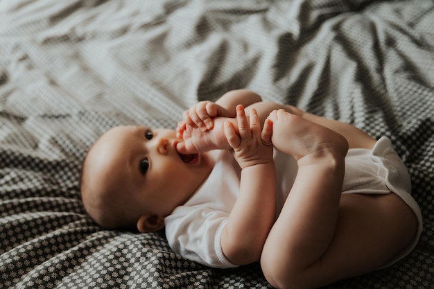 Lindo bebê fofo deitado e brincando na cama na foto do quarto com a luz do dia da janela