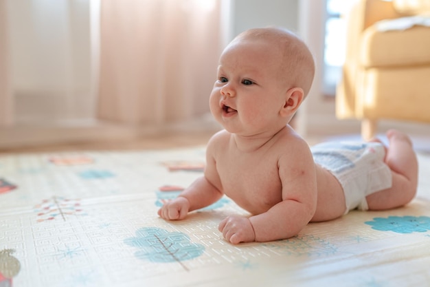 Un lindo bebé gordito yace desnudo en la alfombra y mira felizmente las fotos