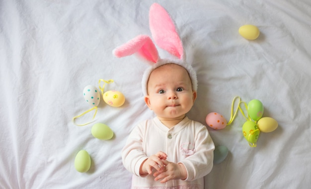 Lindo bebé gracioso con orejas de conejo y coloridos huevos de Pascua en casa sobre un fondo blanco.