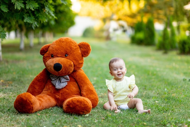 Lindo bebé con gran oso de peluche sobre césped o césped verde en verano