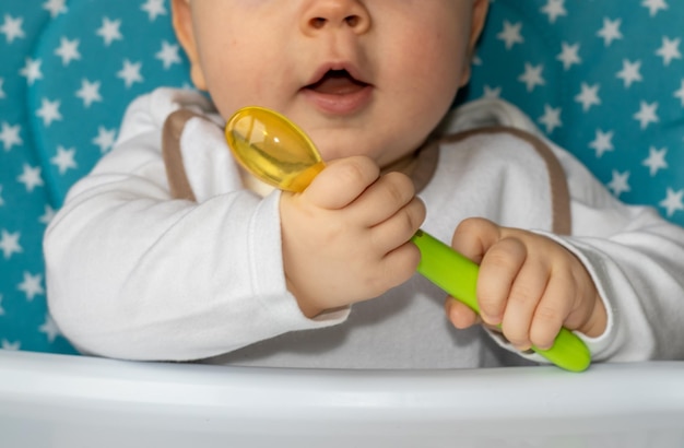 un lindo bebé hambriento está sentado en una silla de alimentación y comiendo frutas o verduras en puré