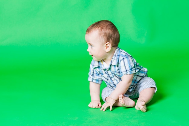 Lindo bebé infantil sentado en el suelo mirando a otro lado, aislado en un fondo verde