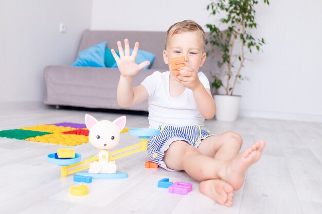 lindo bebé juega con balanzas en casa en el piso y aprende a contar mostrando cinco dedos