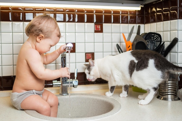 Lindo bebé jugando en el fregadero de la cocina con un gato