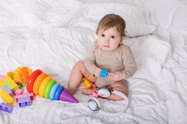 lindo bebé jugando con juguetes coloridos y auriculares en un espacio de banner de manta para texto