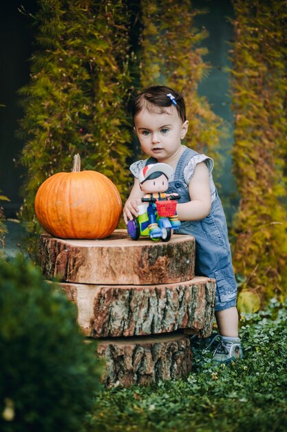 Lindo bebé jugando con su juguete en su patio junto a los tocones decorativos con calabaza grande