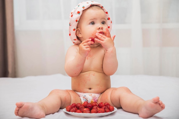 lindo bebé manchado en un sombrero comiendo bayas en la cama