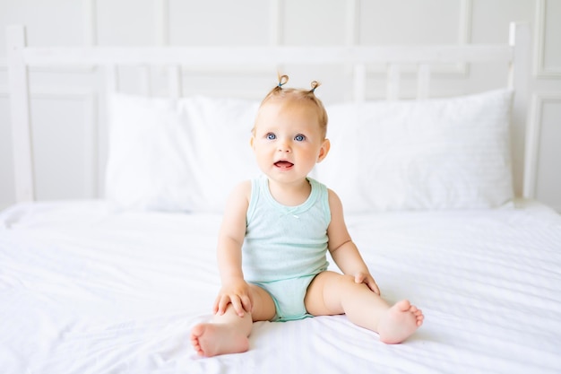 Un lindo bebé con un mono hecho de tela de algodón natural está sentado sobre ropa de cama blanca en el dormitorio Un bebé feliz en la cama Textiles y ropa de cama para niños