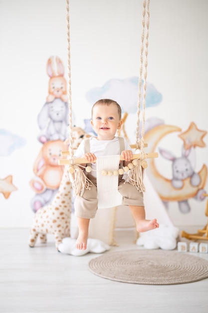 Lindo bebé monta en un columpio de madera en la habitación de los niños en casa juguetes educativos para niños interior de la habitación de los niños