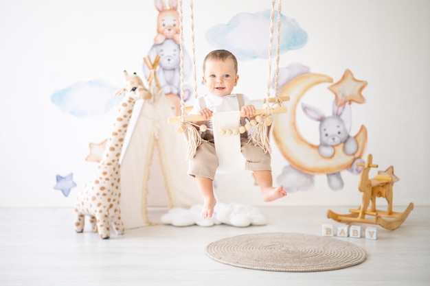 Lindo bebé monta en un columpio de madera en la habitación de los niños en casa juguetes educativos para niños interior de la habitación de los niños