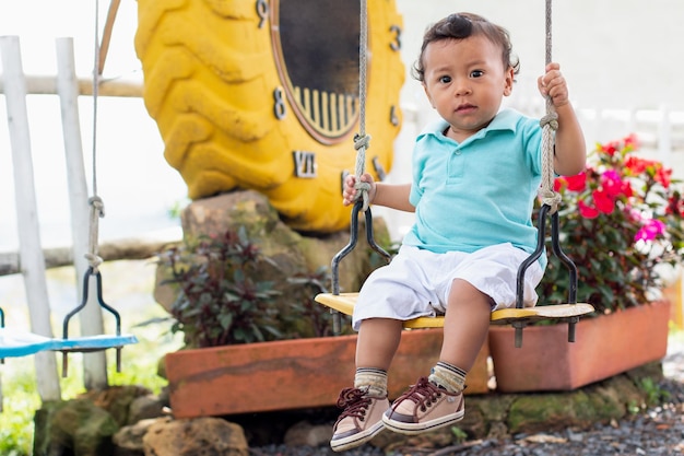 Lindo bebé montando en un columpio en un colorido parque Hermoso niño colombiano de un año jugando