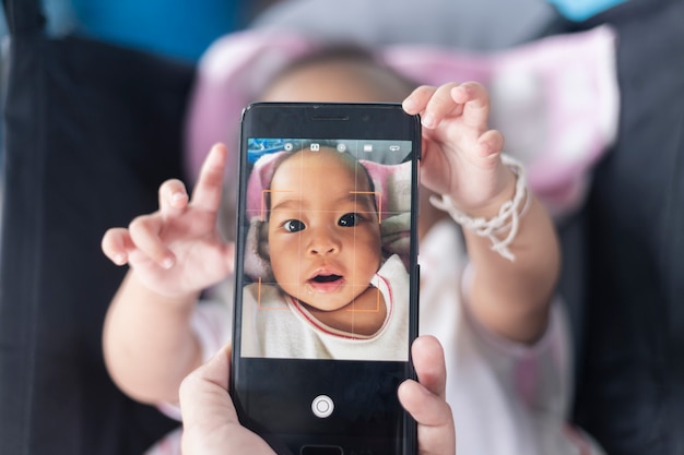 Foto lindo bebé muestra sus propias fotos en el teléfono inteligente en el cochecito.