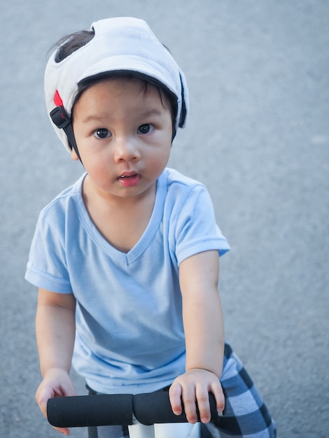 Lindo bebé niño asiático usar casco de seguridad para aprender a montar su primera bicicleta blanca para correr en la carretera