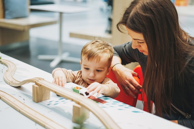 Lindo bebé niño niño pequeño con madre jugar con juguetes para el automóvil en la sala de juegos en el centro comercial