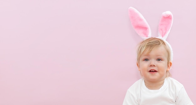 Un lindo bebé con orejas de conejo en un fondo rosa