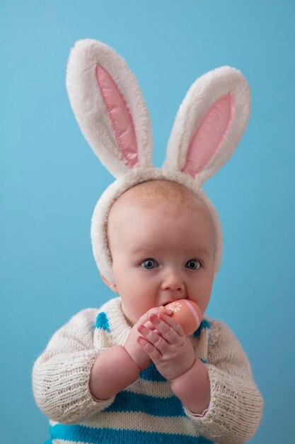 Lindo bebé con orejas de conejo de pascua jugando con un huevo de pascua