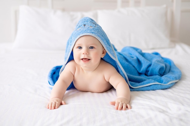 Un lindo bebé que se ríe feliz después de un baño está jugando en una cama blanca en una habitación espaciosa para niños El niño está en una toalla limpia y seca Lavando la higiene del bebé, la salud y el cuidado de la piel