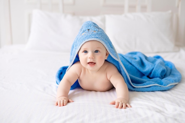 Un lindo bebé que se ríe feliz después de un baño está jugando en una cama blanca en una habitación espaciosa para niños El niño está en una toalla limpia y seca Lavando la higiene del bebé, la salud y el cuidado de la piel