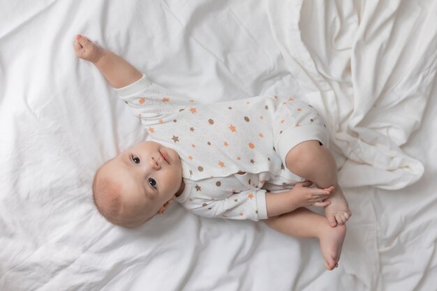 Lindo bebê recém-nascido alegre está deitado de costas em um lençol branco com vista de cima.