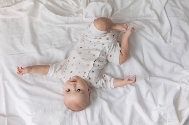 Lindo bebê recém-nascido alegre está deitado de costas em um lençol branco com vista de cima.