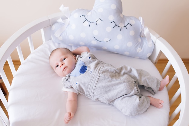 Lindo bebê recém-nascido, deitado em uma cama redonda com belos pára-choques em delicados tons de cinza, azuis e brancos