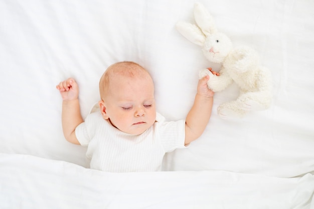 Foto lindo bebê recém-nascido dormindo debaixo de um cobertor abraçando um coelhinho de pelúcia doce bebê saudável dorme em um berço branco um lugar para texto