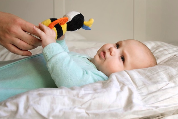 Lindo bebé recién nacido acostado boca arriba y juega con juguetes coloridos Niño pequeño de tres meses toma un juguete Retrato de un niño recién nacido juguetón Concepto de infancia Nueva vida Cuidado del bebé Vista superior