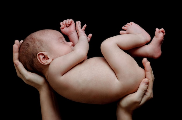 Foto lindo bebé recién nacido acostado en manos de la madre sobre fondo negro