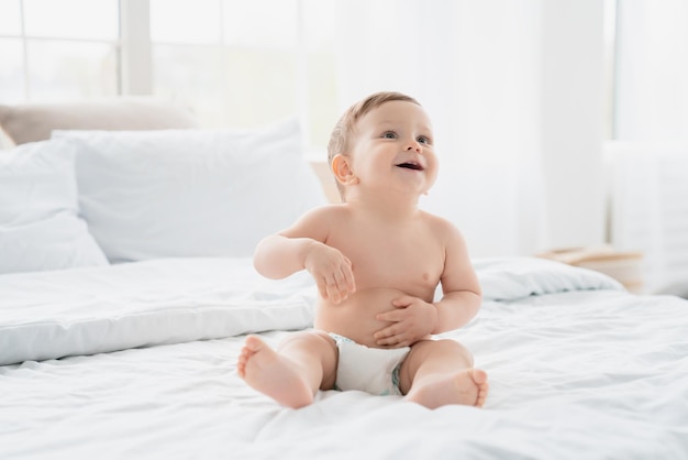 Lindo bebé recién nacido con pañal sentado en una manta blanca en la cama de la guardería Niño niño después de la ducha bebé hija hijo cambio de pañal y cuidado de la piel Concepto de la infancia