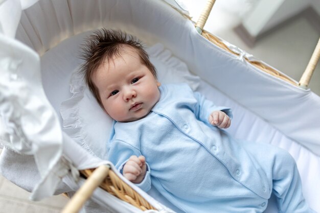 Foto un lindo bebé recién nacido en pijama azul yace en una cuna de paja