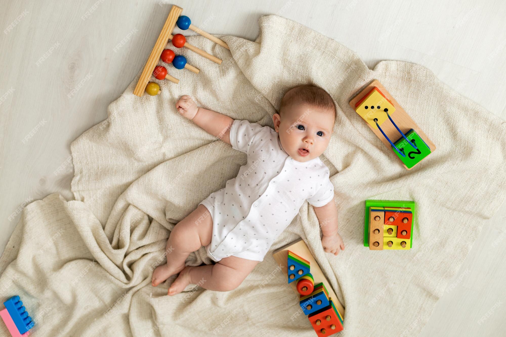 Un lindo bebé recién nacido con ligera está jugando con juguetes educativos tirados en el suelo sobre una manta de lino gris. vista superior. niños. feliz infancia y maternidad. espacio para texto | Foto