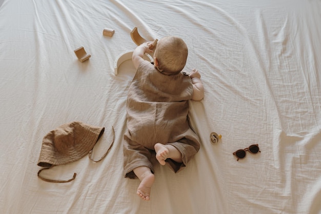 Lindo bebé recién nacido en traje de lino marrón tendido sobre sábanas de cama beige Composición estética de moda para bebés Vista superior plana