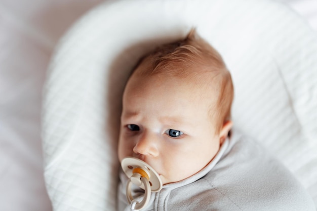 Lindo bebé rubio caucásico de dos meses de edad acostado en un capullo en casa y chupando el pezón de una persona