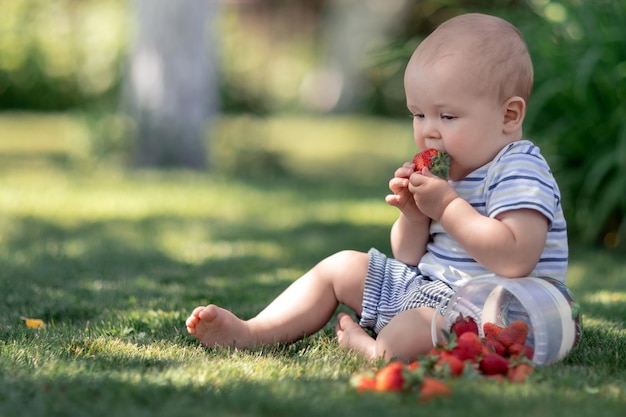 Lindo bebé sentado en el césped en el jardín y saborea fresas