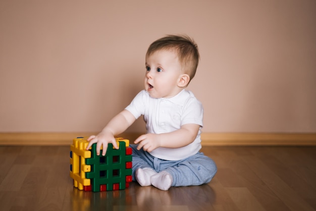 Lindo bebé sentado en el piso de la casa jugando con un cubo multicolor