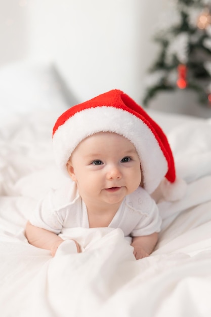 lindo bebé con sombrero de Santa en casa en la cama. El primer Año Nuevo. Regalo de Navidad