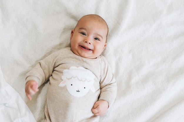 Lindo bebé sonriente de 46 meses en general beige en los tonos naturales de la cama