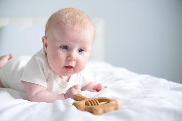 Lindo bebé sonriente acostado boca abajo en la cama de los padres jugando con mordedor de madera