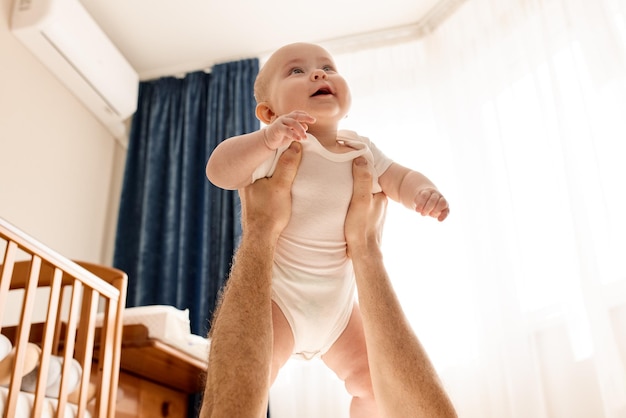 Un lindo bebé sonriente alegre en los brazos extendidos de su padre que yace en el suelo en un brillante