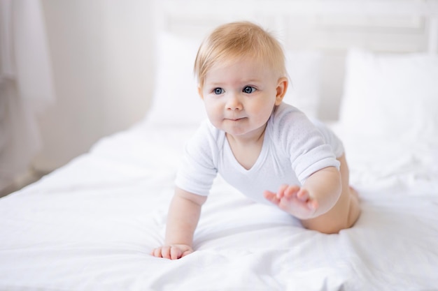 Lindo bebé sonriente aprende a gatear en una cama blanca en casa pequeño bebé rubio se despertó en la mañana feliz infancia y familia