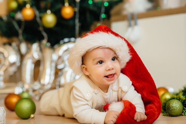 Lindo bebé sonriente está acostado bajo un árbol de Navidad festivo y jugando con regalos